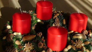 Red candles on decorative wreath with pinecones.