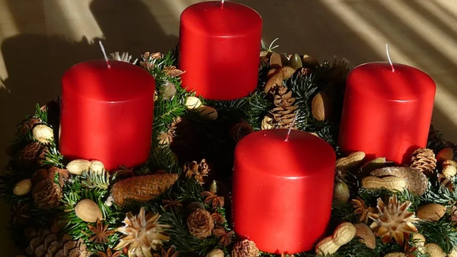 Red candles on decorative wreath with pinecones.